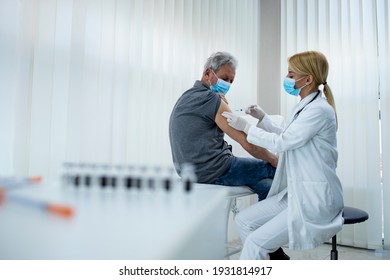 An Elderly Man Getting Vaccine Shot By Doctor Epidemiologist In Hospital Office During Corona Virus Pandemic. Immunization Of Older Population.