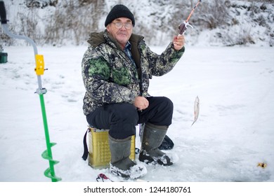 Elderly Man With Glasses, Fishing In Winter, Pulls Fish Out Of The Ice