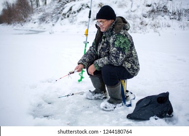 Elderly Man With Glasses, Fishing In Winter, Pulls Fish Out Of The Ice