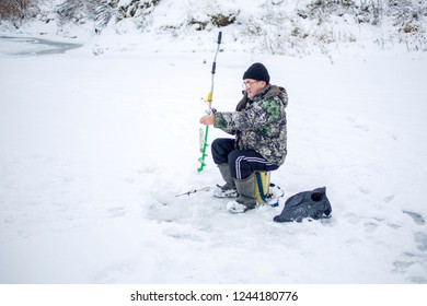 Elderly Man With Glasses, Fishing In Winter, Pulls Fish Out Of The Ice