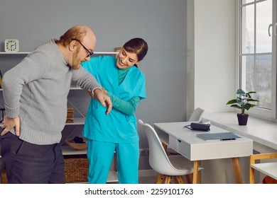 Elderly man with glasses, walking holding the small of his back with caring nurse. Beautiful, smiling, young nurse supports and helps old man with back pain to reach chair. Healthcare concept. - Shutterstock ID 2259101763