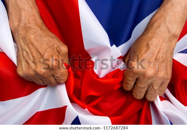 Elderly man hands holding a UK flag. The\
concept of caring for\
pensioners.