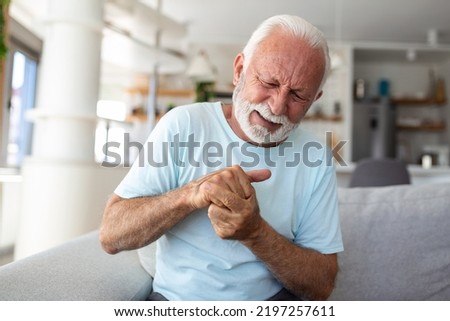 Elderly man has pain in fingers and hands. Old man with finger pain, Man massaging his arthritic hand and wrist.