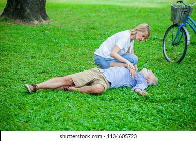 Elderly Man Have Chest Pains Or Heart Attack Fall Lay Down On Grass Floor  Old Woman Come To The First Aid  In The Park, Health Care Concept.