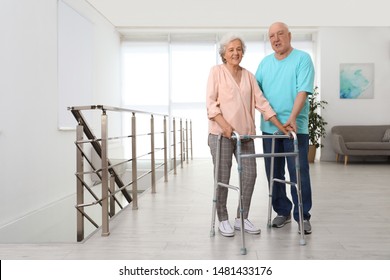 Elderly Man Helping His Wife With Walking Frame Indoors