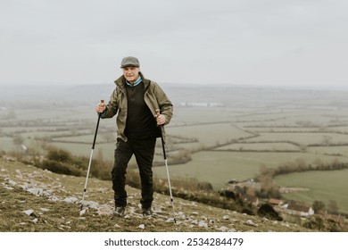 Elderly man hiking with poles on grass hill. Outdoor activity in nature. Senior enjoying hiking in nature landscape. Scenic landscape. Senior man hiking, outdoor activity in nature grass hill - Powered by Shutterstock