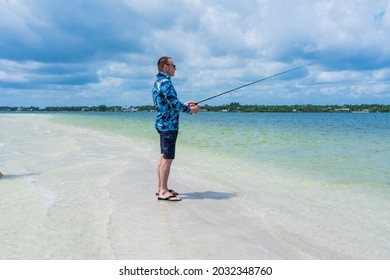 An Elderly Man In His 60s Holds A Fishing Rod While Fishing On A Sandbank In The Salt Water Of The Ocean On Indian River Island, Florida.