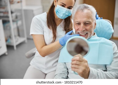 Elderly man and his young female dentist smiling while looking in the mirror in dental clinic - Powered by Shutterstock