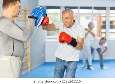 Elderly man hitting the focus mitts held by his boxing trainer - Powered by Shutterstock