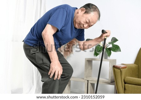 An elderly man holding a cane while holding his knees
