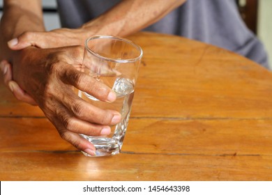 Elderly man is holding his hand while drinking water because Parkinson's disease.Tremor is most symptom and make a trouble for doing activities such as eat or drink.Health care or elderly concept.