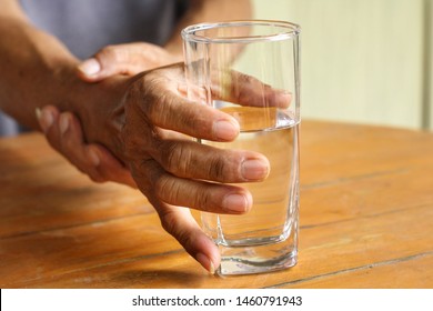 Elderly man is holding his hand while drinking water because Parkinson's disease.Tremor is most symptom and make a trouble for doing activities such as eat or drink.Health care or elderly concept.