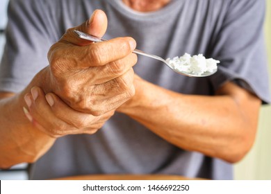 Elderly man is holding his hand while eating because Parkinson's disease.Tremor is most symptom and make a trouble for doing activities such as eat.Health care or elderly concept.Selective focus. - Shutterstock ID 1466692250