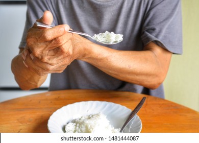 Elderly man is holding his hand while eating because Parkinson's disease.Tremor is most symptom and make a trouble for doing activities such as eat.Health care or elderly concept.Front view.