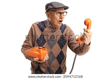 Elderly man holding an old vintage rotary phone and looking at the handset isolated on white background