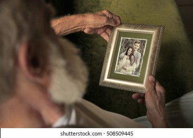 Elderly Man Holding Photo Frame With Picture Of Young Couple. Happy Memories Concept.