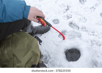 An Elderly Man Is Ice Fishing And He Is Holding The Jig In His Hand.