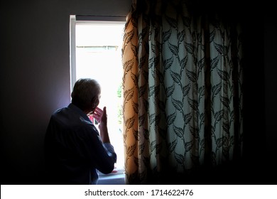 
Elderly man indoors in the house looks out the window. Loneliness.  Corona virus. Stay at home, stay safe