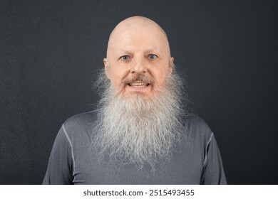 Elderly man with a long, white beard smiling widely against a dark background. His bright eyes and bald head emphasize his cheerful and friendly demeanor - Powered by Shutterstock