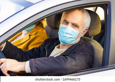 An Elderly Man In A Medical Face Mask Driving A Car. Coronavirus Pandemic Concept. Road Trip, Travel And Old People Concept - Happy Senior Couple Driving In Car