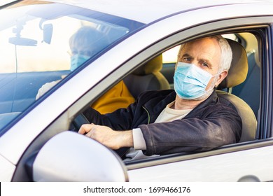 An Elderly Man In A Medical Face Mask Driving A Car. Coronavirus Pandemic Concept. Road Trip, Travel And Old People Concept - Happy Senior Couple Driving In Car