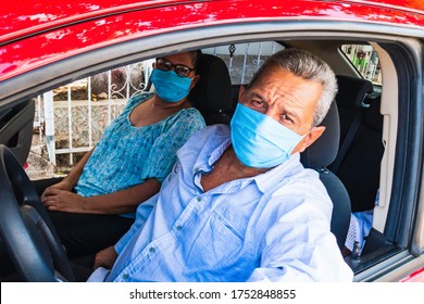 An Elderly Man In A Medical Face Mask Driving A Car. Coronavirus Pandemic Concept. Road Trip, Travel And Old People Concept - Happy Senior Couple Driving In Car