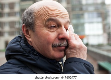 An Elderly Man With A Mustache And Bald Head Wipes Tears In His Eyes From The Wind