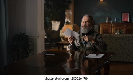 Elderly Man Opening Envelope With Knife In Ancient Cabinet. Old Man Reading Letter In Luxury House. Senior Business Man Working With Correspondences At Table In Home Office