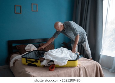 Elderly man packing clothes into a suitcase on bed, preparing for travel. Focus on packing process in cozy bedroom setting, symbolizing adventure and life experiences ahead. - Powered by Shutterstock