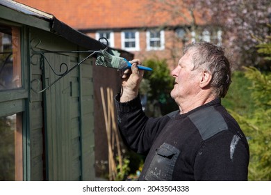 An Elderly Man Painting A Garden Shed With Preservative Paint