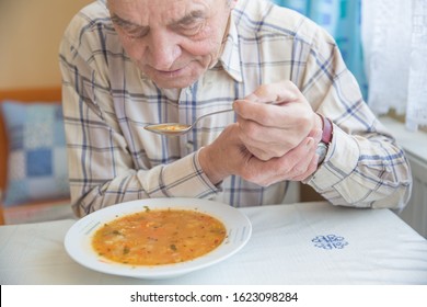 Elderly man with Parkinsons disease holds spoon in both hands.