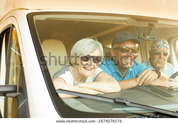 Elderly man with a patterned\
bandana and sunglasses looking out of the tailgate of his\
camper