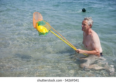 Elderly Man Is Playing In The Sea With A Fishing Net