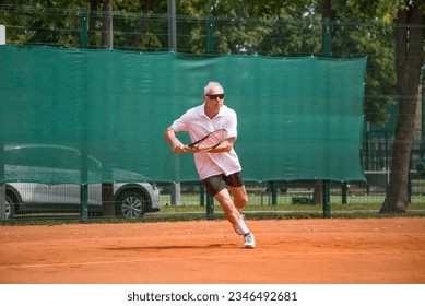 An elderly man playing tennis runs to take the ball. Open ground. - Powered by Shutterstock