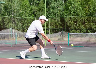 An elderly man plays tennis on an outdoor court - Powered by Shutterstock