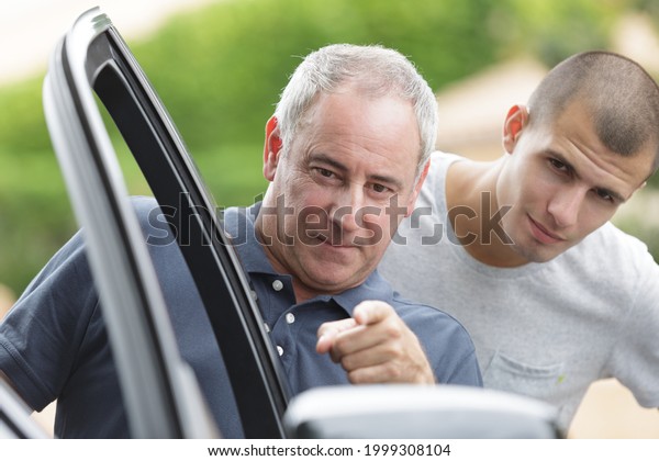 elderly man pointing at\
cars side mirror