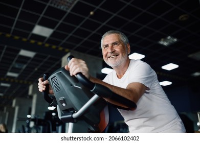 Elderly man poses on exercise bike in gym