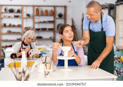 elderly man potter teaches young girl to make clay products - Powered by Shutterstock