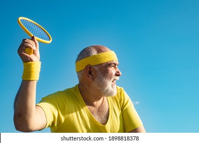 Elderly man practicing tennis on blue sky background. Senior man tennis player serving - Powered by Shutterstock