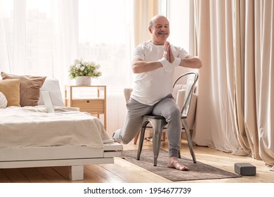 Elderly man practicing yoga asana warrior using chair