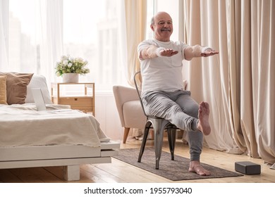 Elderly man practicing yoga asana or sport exercise for legs and hands on chair - Shutterstock ID 1955793040