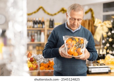 Elderly man prepares to celebrate Christmas by choosing sweet tangerines in the produce section of a supermarket - Powered by Shutterstock