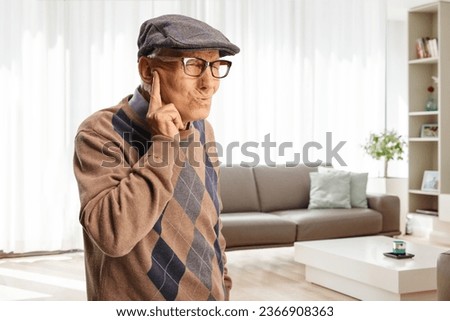 Elderly man protecting his ear from an unpleasent sound at home in a living room