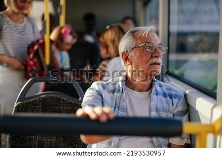 An elderly man is in a public transport bus sitting and looking through the window