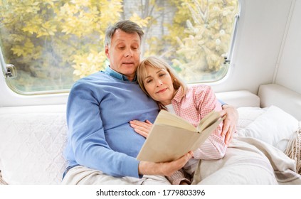 Elderly Man Reading Book To His Peaceful Wife In Bed Inside Of Motorhome On Camping Trip, Panorama