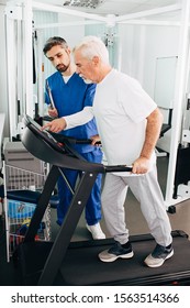 Elderly Man Is Recovering On A Treadmill. His Physiotherapist Helps Him Recover His Body After Physical Injury.