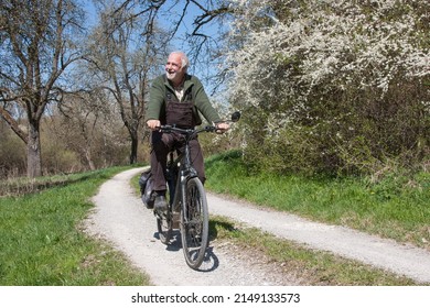 Elderly man rides his bike on a dirt road, past blooming sloe bushes and is happy about the wonderful spring day in difficult times.