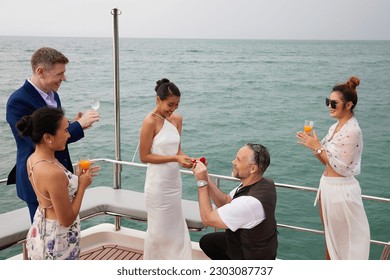 elderly man showing engagement ring and surprise his girlfriend and friends joined in congratulations or success in a party on luxury yacht - Powered by Shutterstock