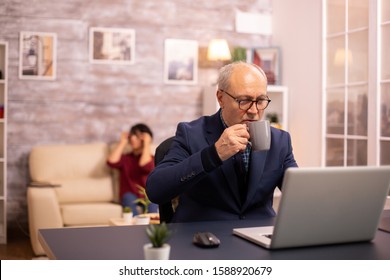 Elderly man sips coffee while working on a latop in modern cozy living room - Powered by Shutterstock