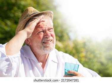 An elderly man sits outside in the great heat. He sweats and drinks mineral water.